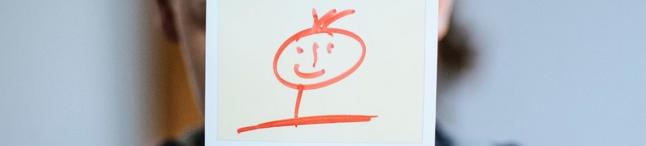 A person holding a photo with a simple red stick figure drawing of a smiling face in front of their own face.