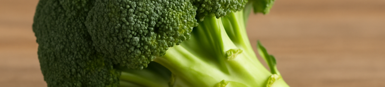 Fresh broccoli with green florets and stalk on a wooden surface.