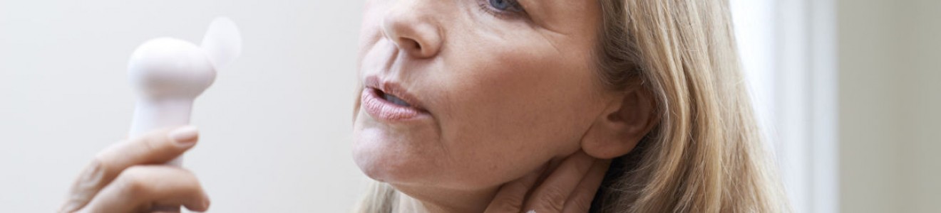 A middle-aged woman holding her neck and looking at a small handheld fan.