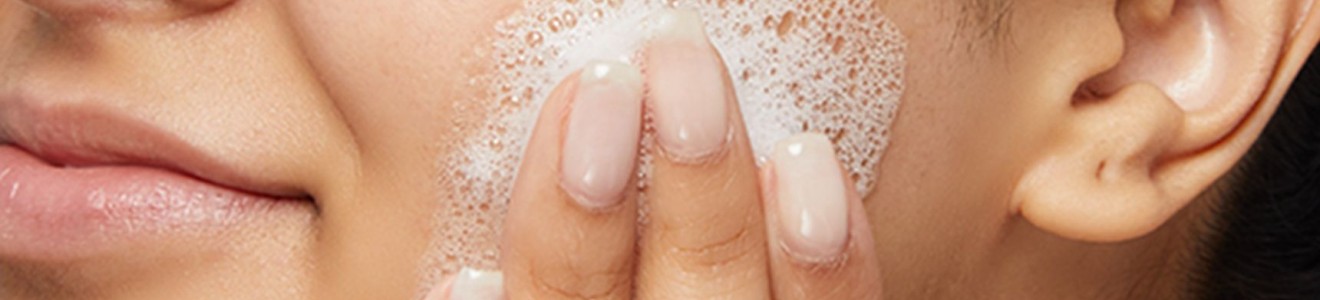 Close-up of a person washing their face with foamy cleanser.