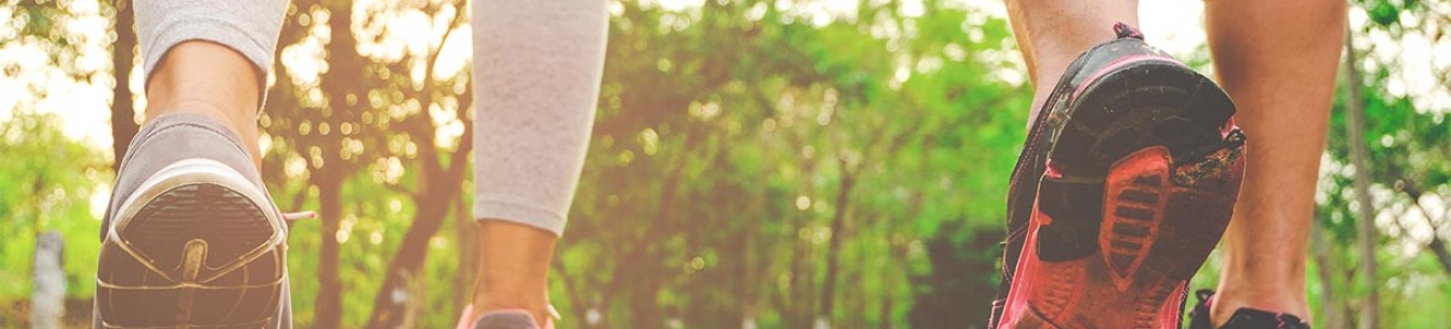 Two people walking on an outdoor paved path surrounded by trees during sunset.