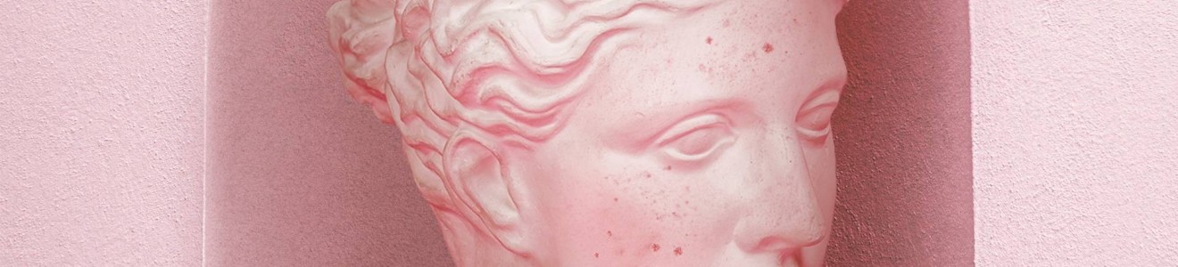 A pink-toned classical-style bust of a woman with wavy hair and a headband displayed in a pink niche.