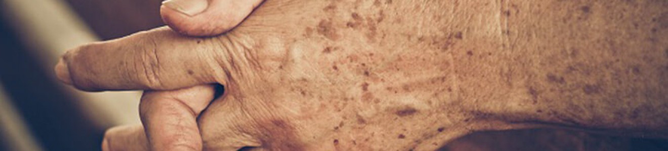 A close-up of elderly hands clasped together resting on a wooden surface.