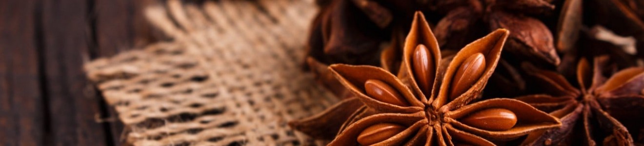 Close-up of star anise spices on a piece of burlap fabric over a wooden surface.