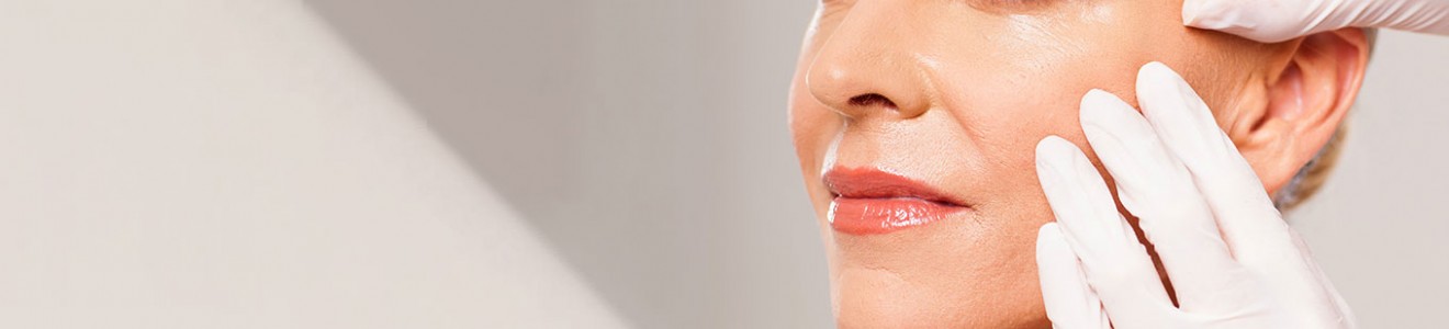 A close-up of a woman receiving a facial treatment from a person wearing white gloves.