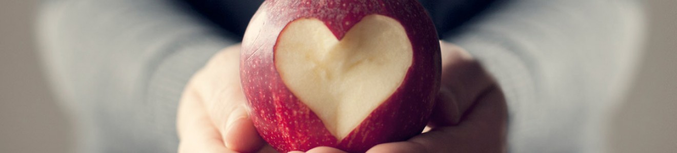 Hands holding a red apple with a heart shape carved into its skin.