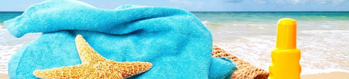 A yellow starfish on a folded blue towel with a woven bag and yellow sunscreen bottle by the beach and ocean waves in the background.
