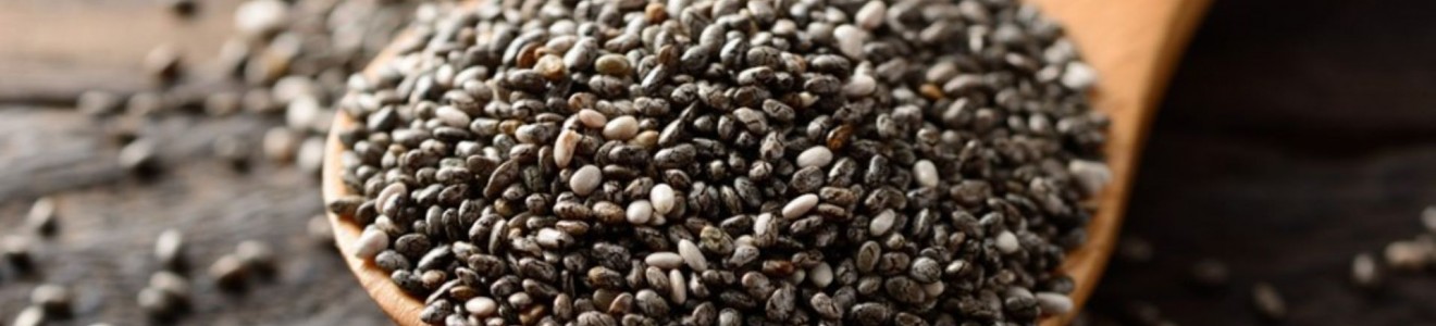 Close-up of a wooden spoon filled with black and white chia seeds on a wooden surface.