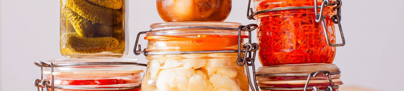 Jars of assorted pickled vegetables, including cucumbers, cauliflower, and carrots, arranged on a wooden surface.