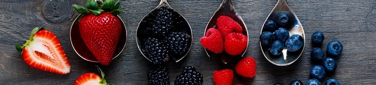 Four spoons with fresh strawberries, blackberries, raspberries, and blueberries arranged on a wooden surface.