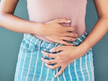 Person in striped denim pants and a pink shirt holding their stomach.