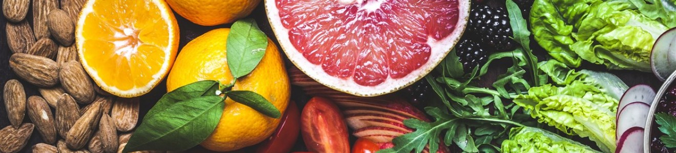 A colorful assortment of fresh fruits, vegetables, nuts, and a bowl of hummus on a dark surface.