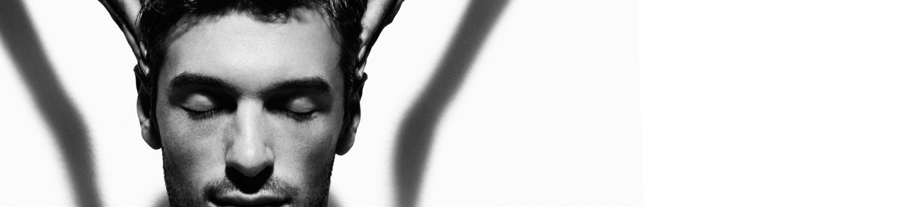 Black and white image of a shirtless man with eyes closed receiving a head massage.