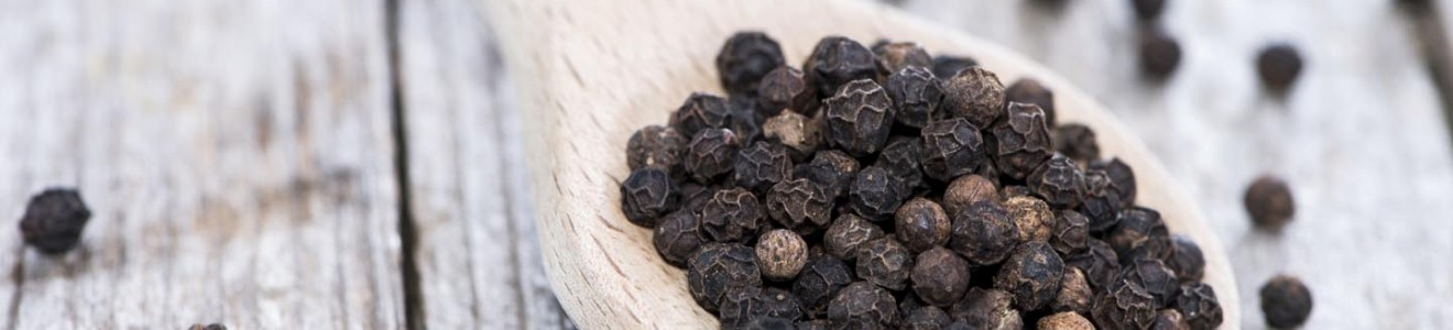 Wooden spoon filled with black peppercorns on a rustic wooden surface.