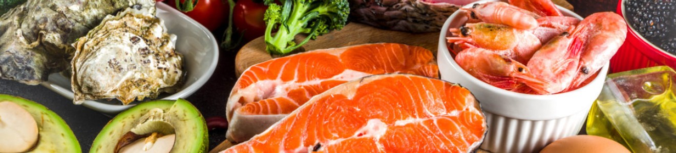 A variety of fresh foods including salmon, shrimp, eggs, avocado, tomatoes, broccoli, oysters, and blackberries.