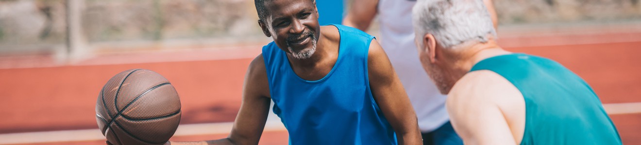 Two older men playing basketball outdoors, one holding the ball and smiling.