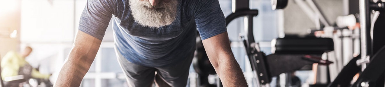 An elderly man with a beard doing push-ups in a gym.