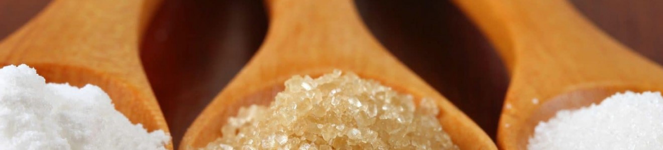 Close-up of three wooden spoons containing different types of salt and sugar with the text 