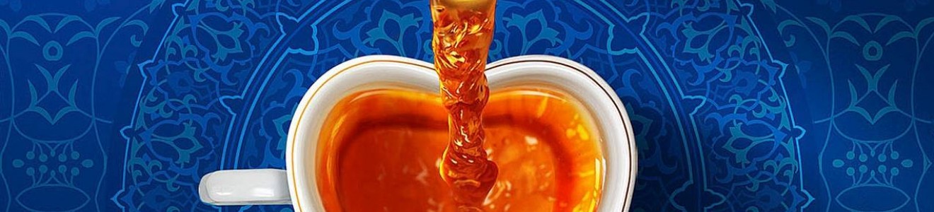 A top-down view of tea being poured from a white teapot into a heart-shaped cup on a blue patterned surface.