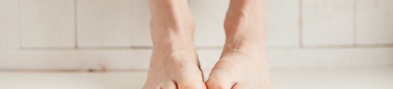 Close-up of bare feet with curled toes pressed against a white floor and wall.