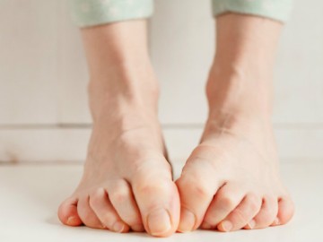 Close-up of bare feet with curled toes pressed against a white floor and wall.