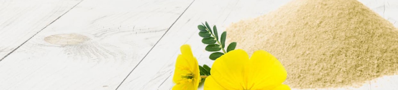 A pile of beige powder next to a yellow flower and green seed pods on a white wooden surface.