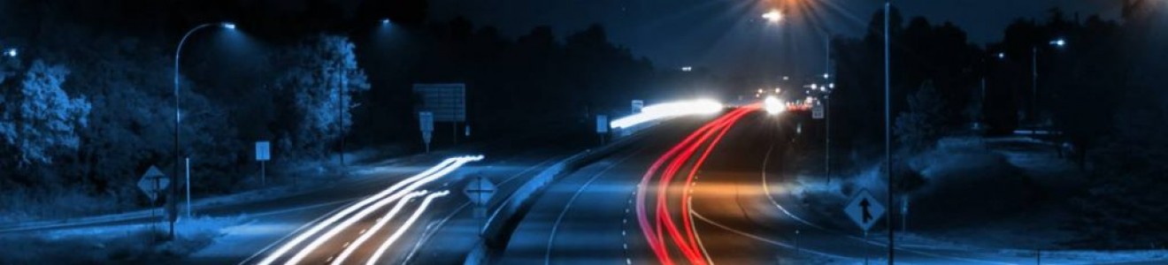 Long-exposure photo of a highway at night showing white and red light trails from moving vehicles.